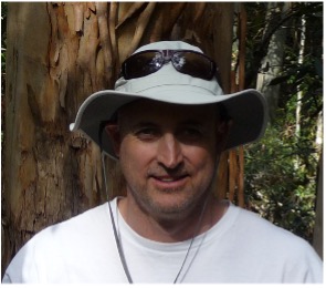 Chris Chaston, in a bucket hat, photographed in front of a tree