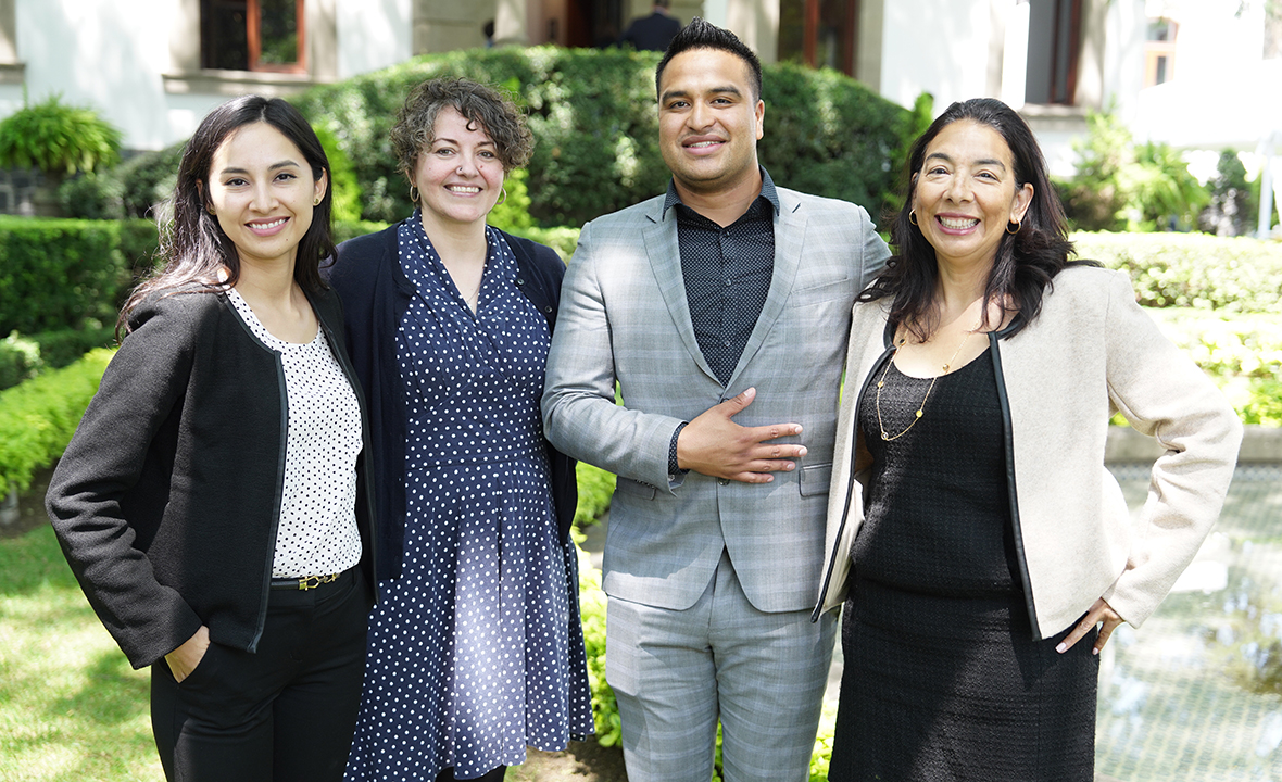 Three women and a man pose for a photo outside in professional clothes