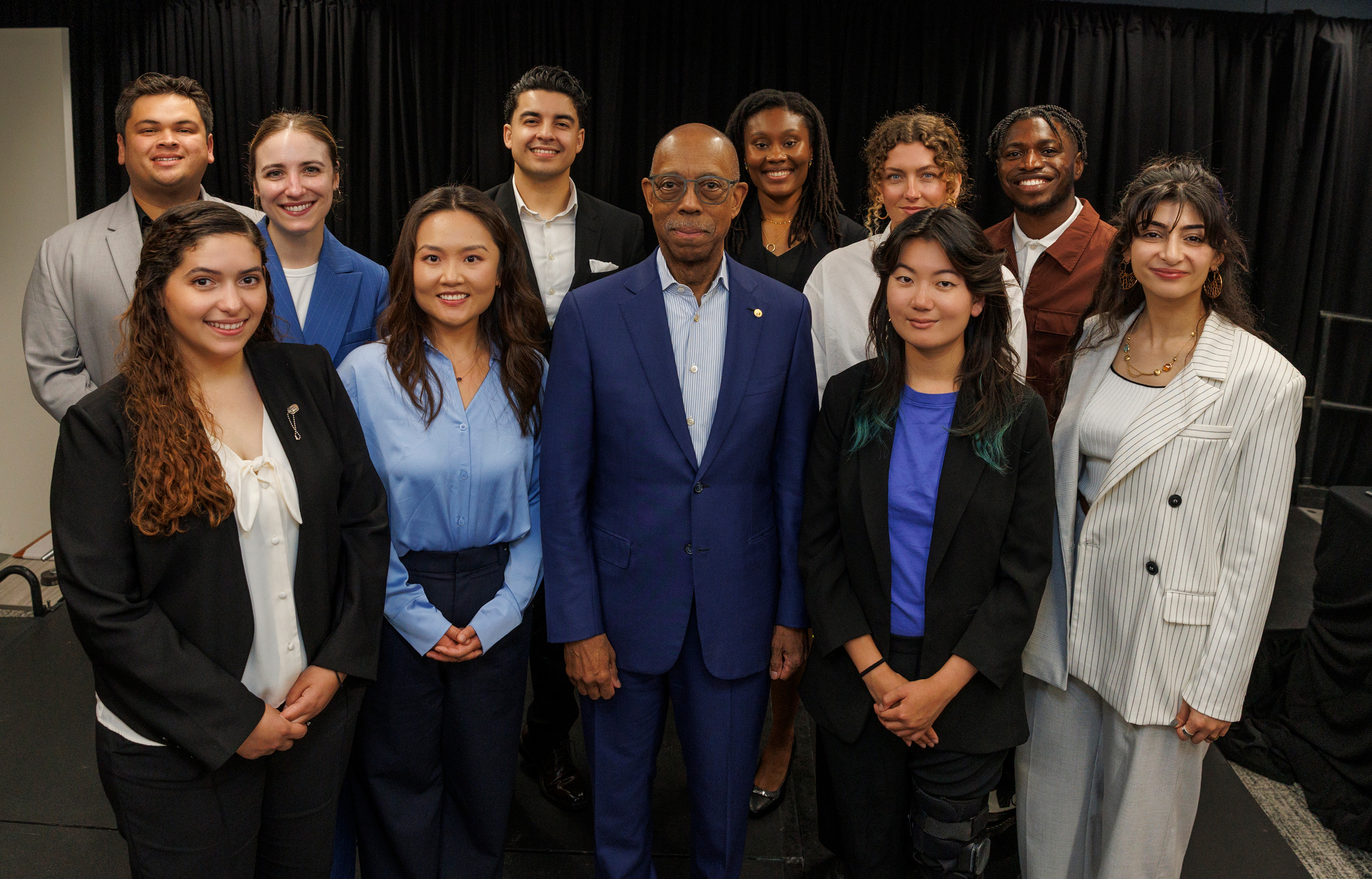 Grad Slam contestants around President Drake, center, in a group photo with a black curtained background