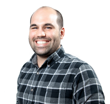 Dominic Milano smiles at the camera wearing a black and gray flannel against a white background