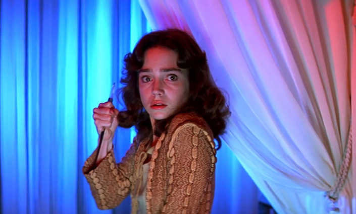 A woman acting in a horror film, looking both frightened and alert, clenches a weapon as if bracing for attack