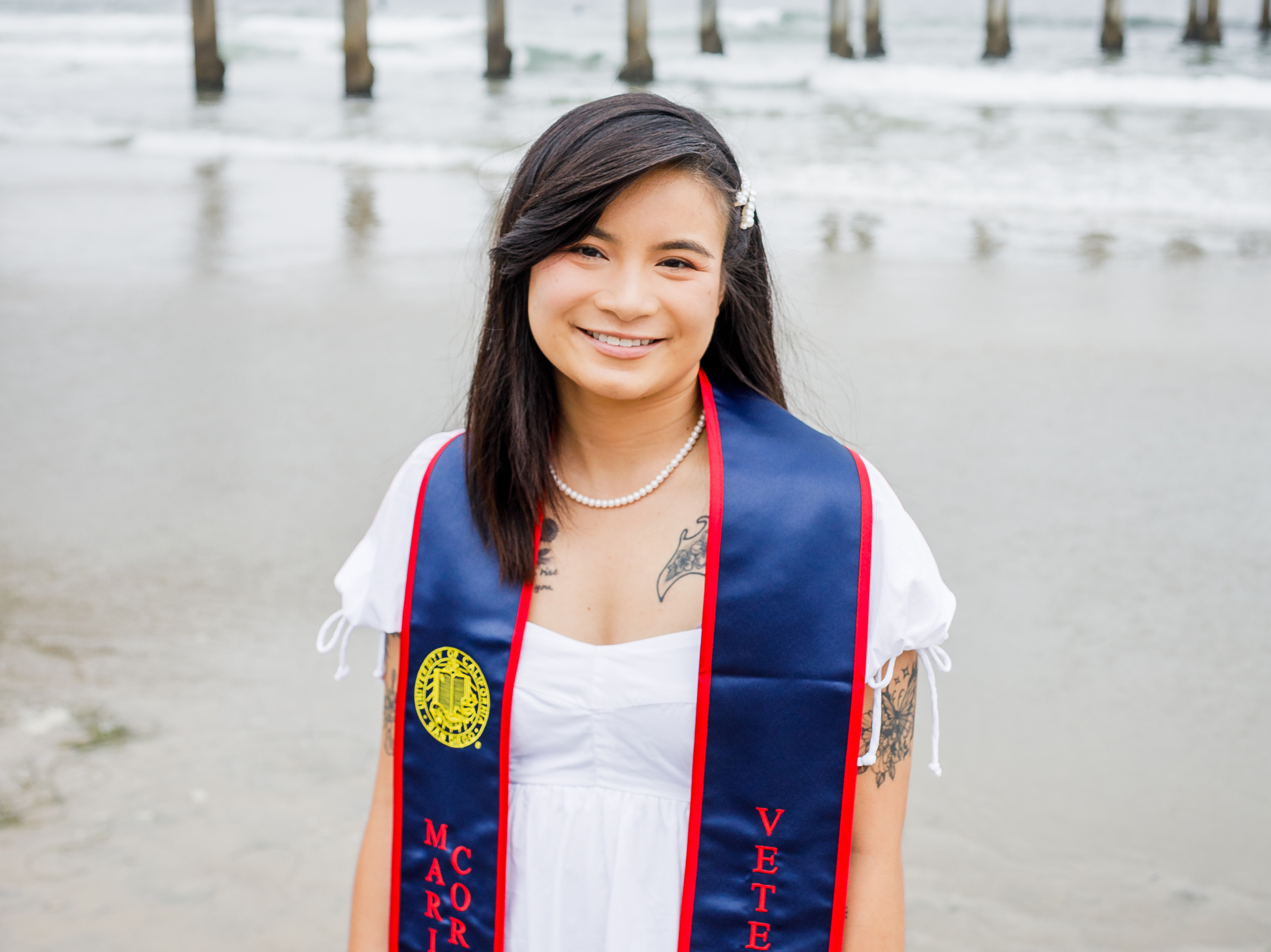 portrait of Hanh Dinh in front of the Scripps Pier wearing her UC San Diego Marine Corps Veteran graduation sash