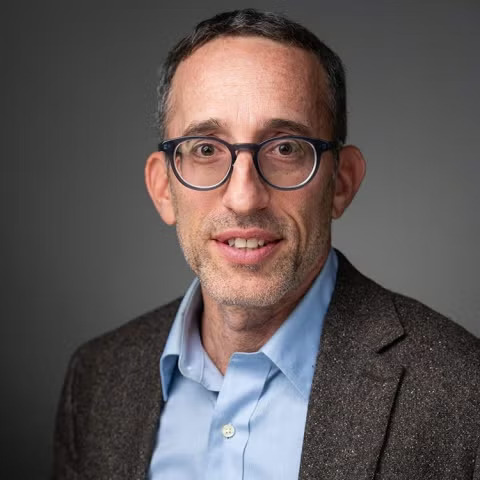 Man with glasses and a dress shirt and jacket smiles at camera