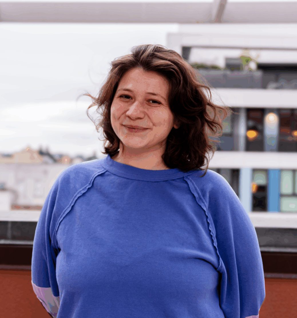 A woman in a blue shirt smiles on a rooftop outdoors