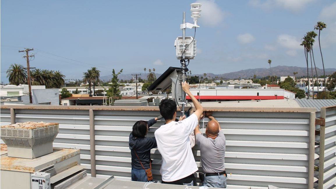 Three people install an air quality monitor in Los Angeles