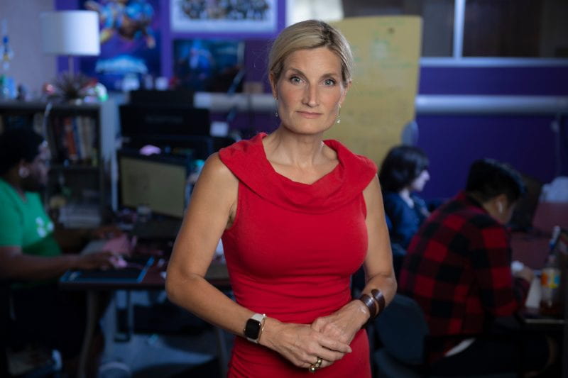 Woman in red dress with hands clasped as people game online behind her out of focus