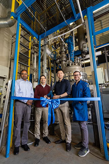 Four men stand in front of a piece of large equipment in a lab