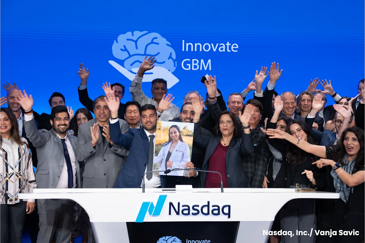 A group of people at NASDAQ surround someone holding a portrait of a young doctor