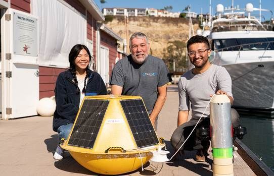 Three people pose with a buoy on a dock