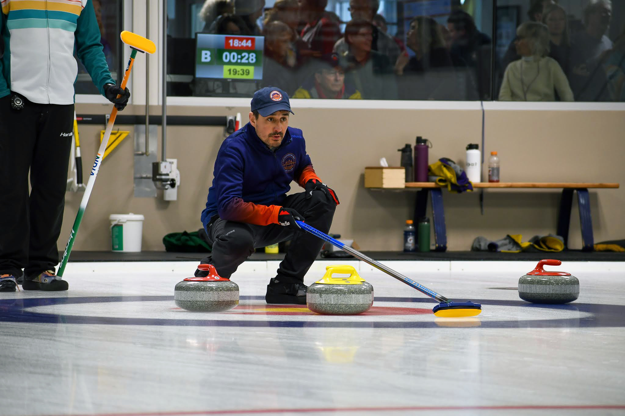 A man bending down on one knee looking at where to aim the stones in curling