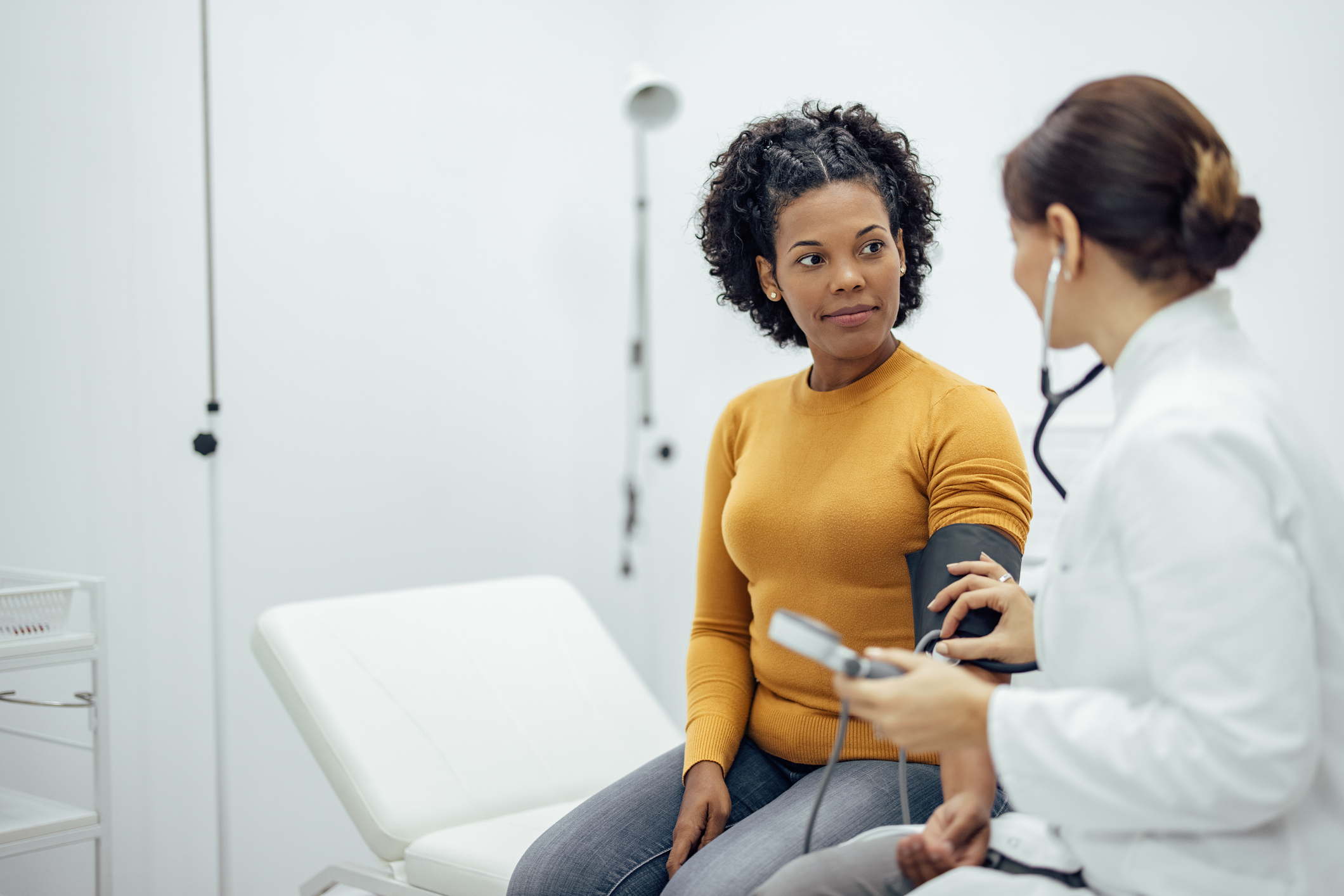 A woman in a yellow sweater is talking with a doctor in an exam room