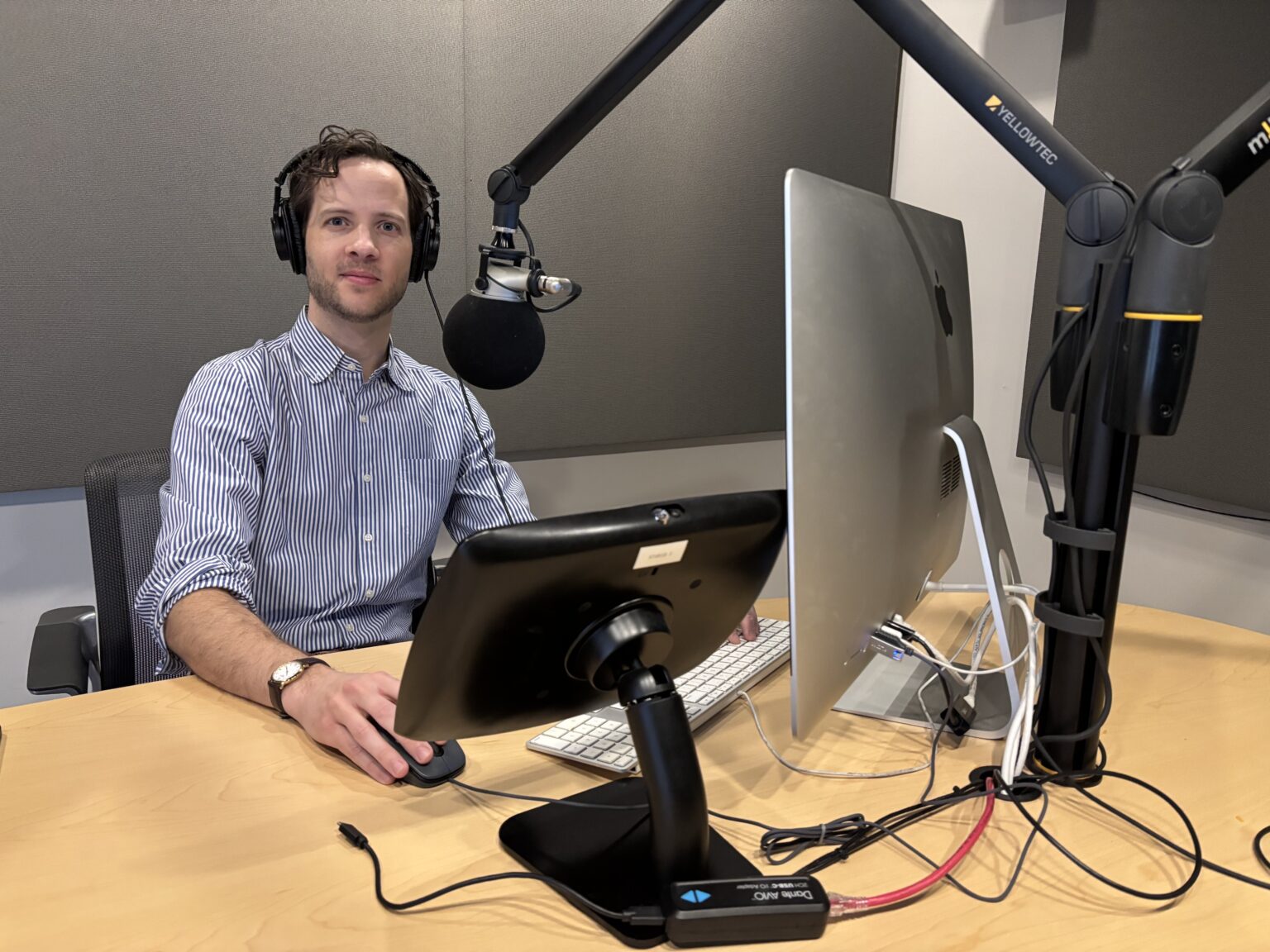 A man with headphones and a microphone in front of a computer in a podcast studio