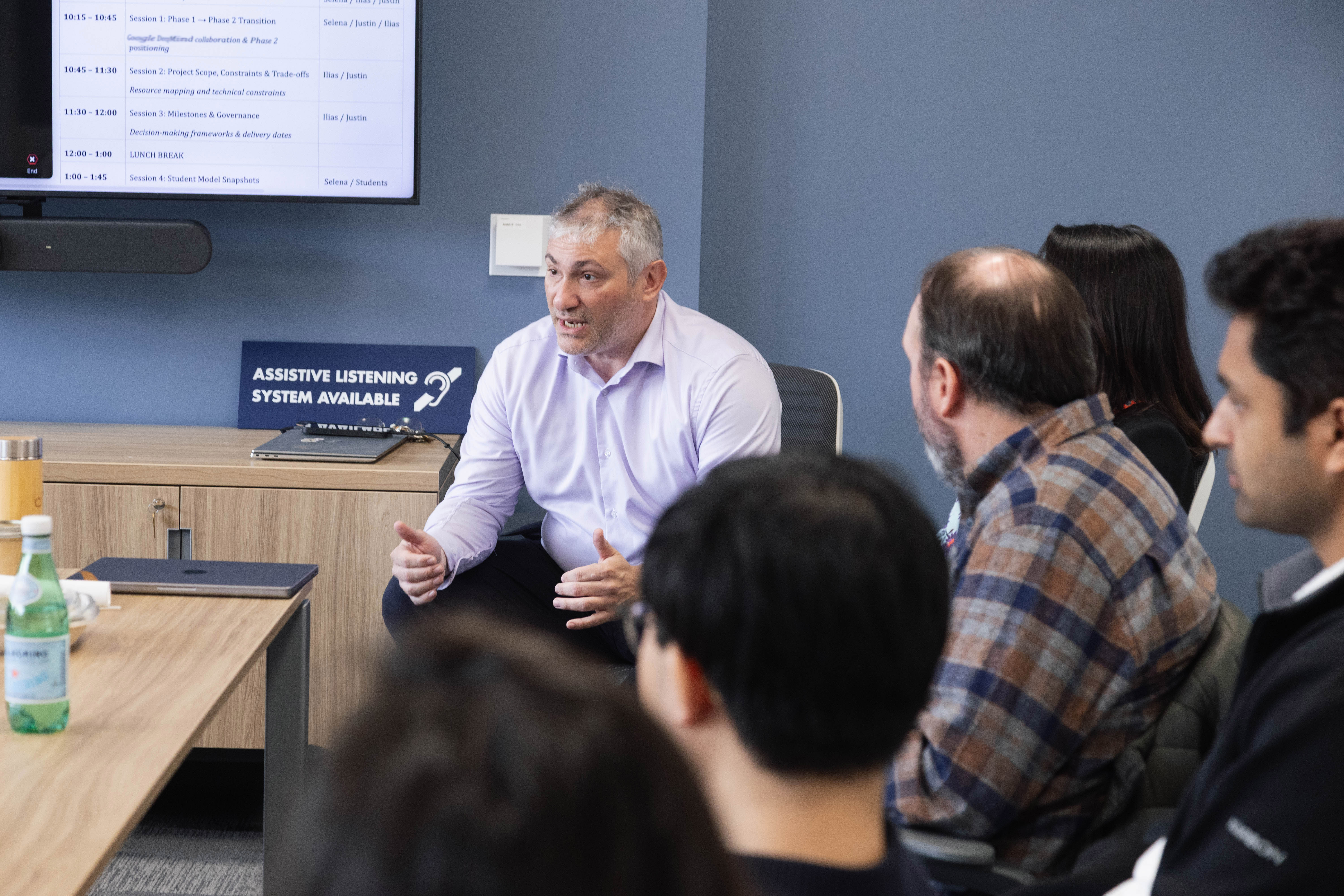 A man seated at a conference table talking to other people at the table