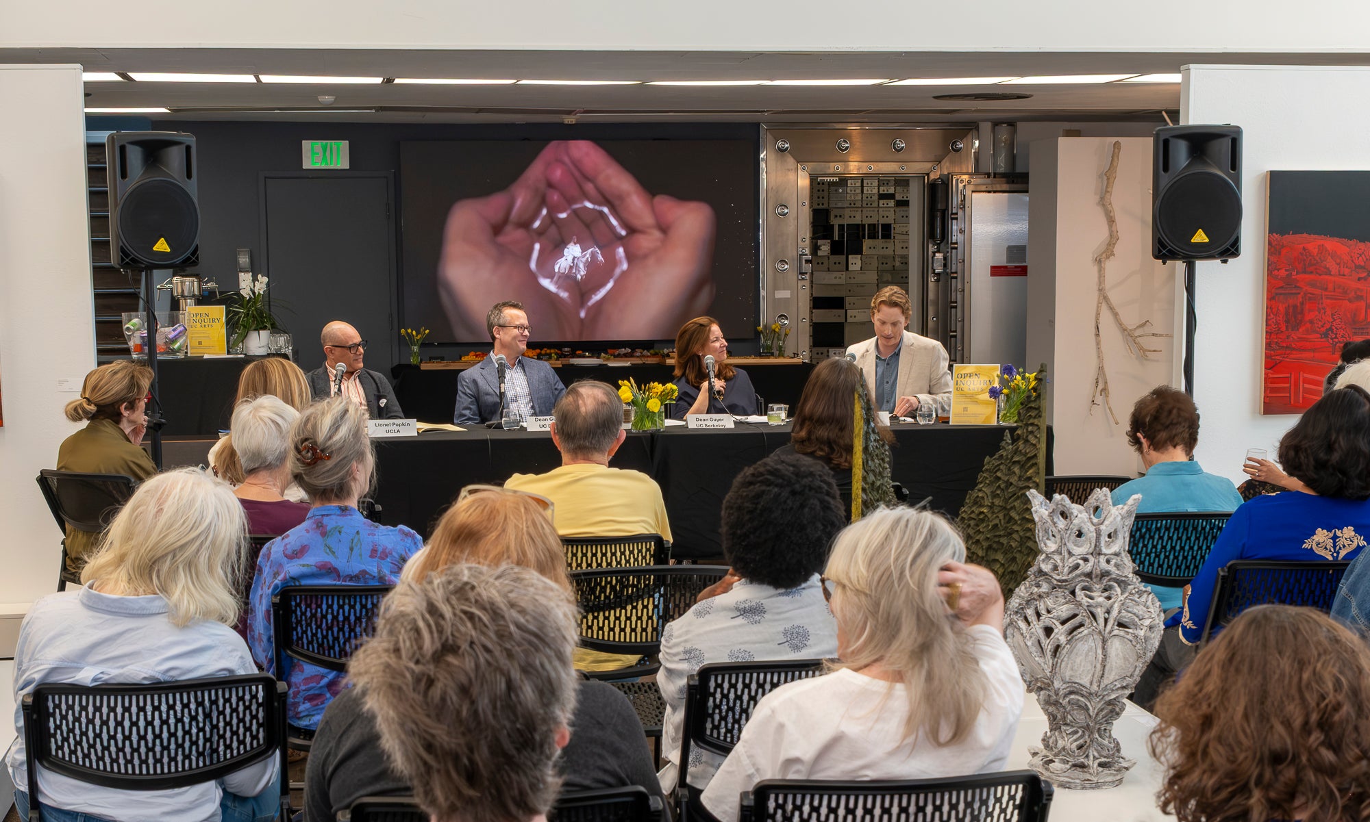 A shot of a crowd facing a table with four people sitting at it in an art gallery