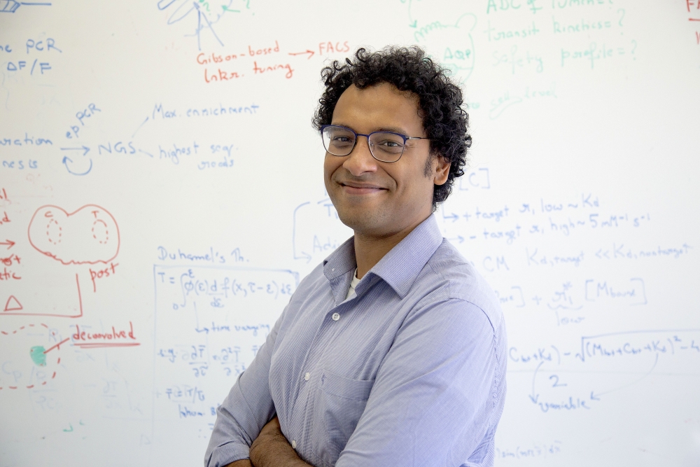 A professor smiles in front of a whiteboard with a lot of writing and calculations on it