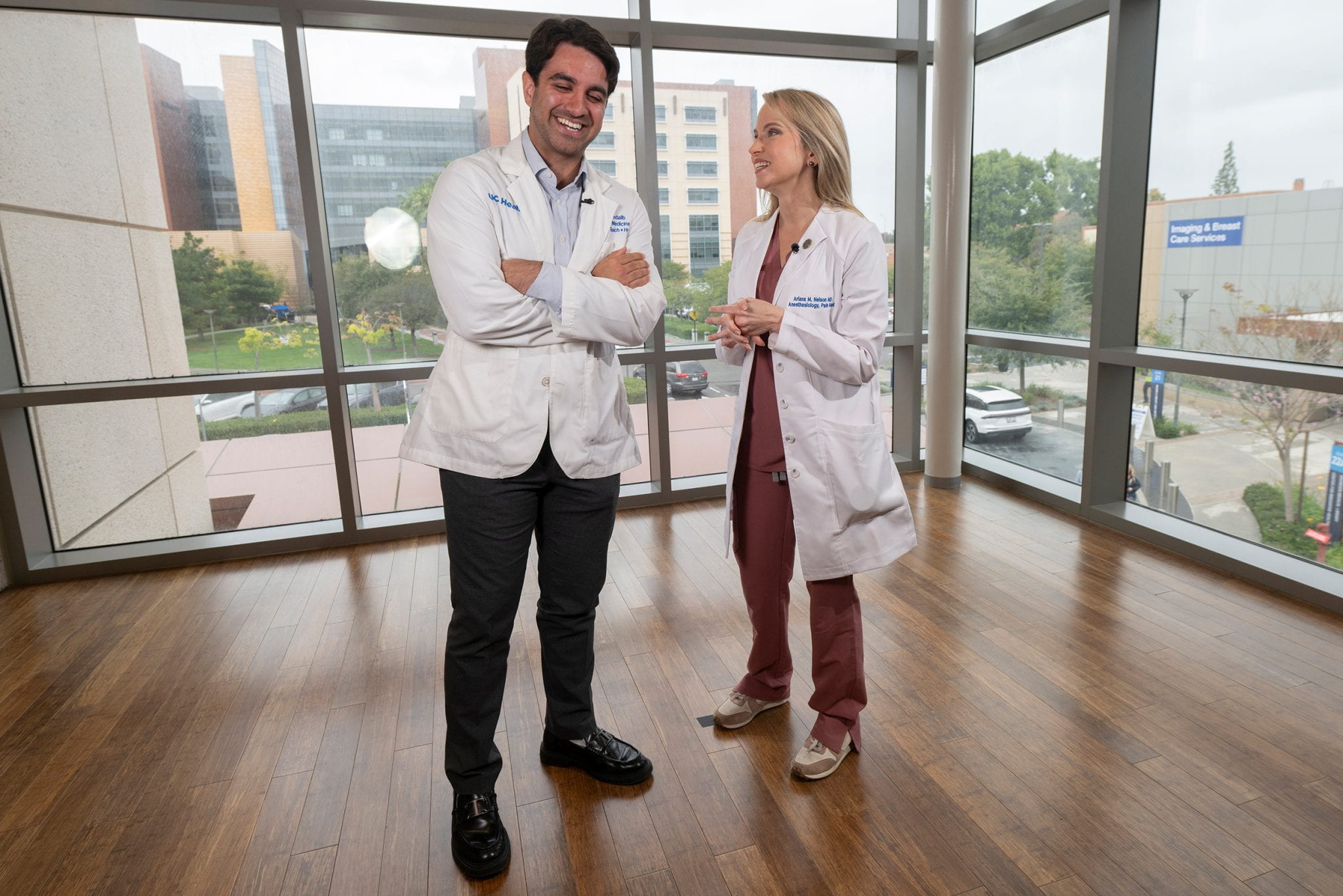 A man in a white medical jacket grins while talking with a woman in a white medical jacket