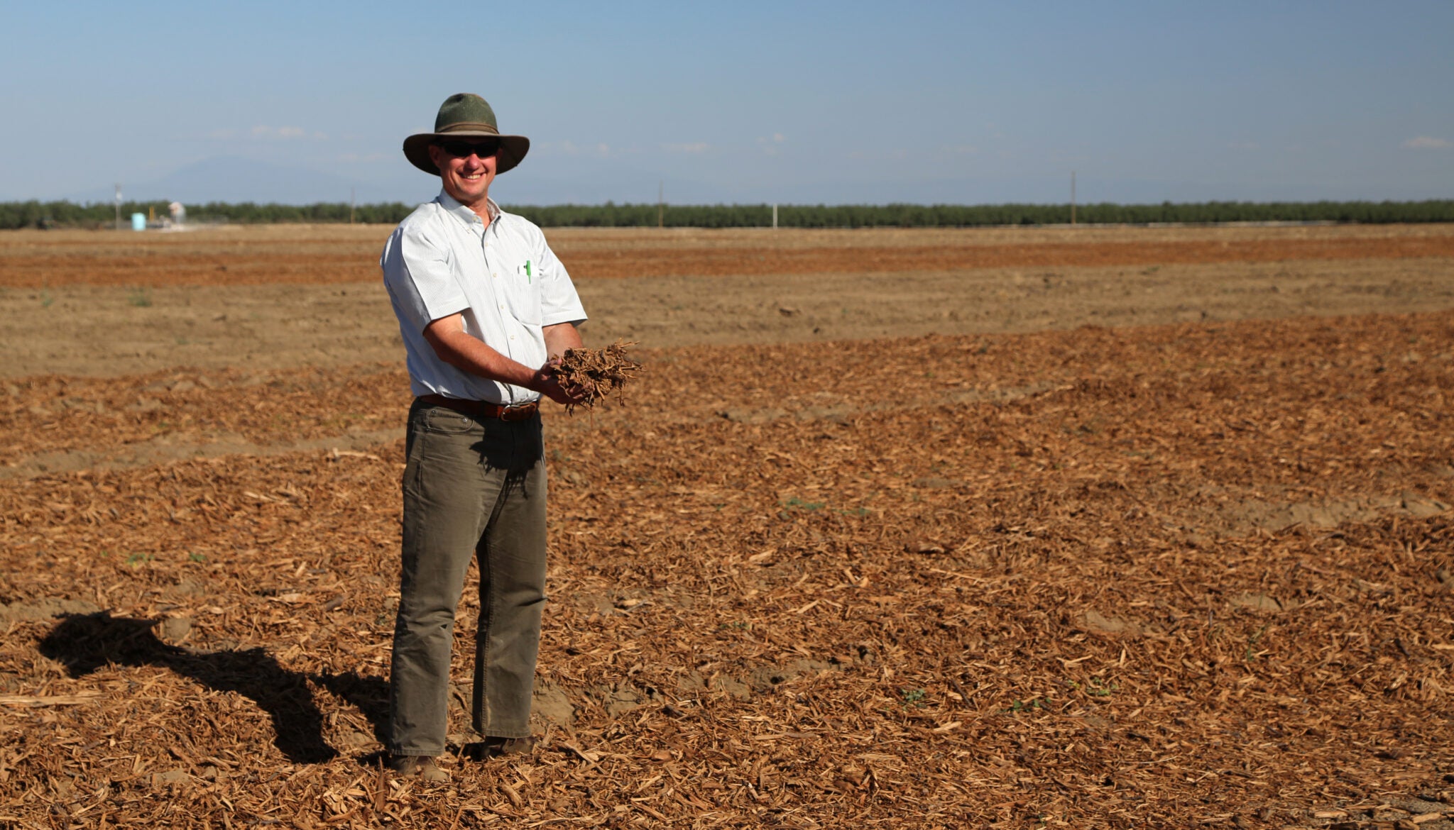 A farmer holds up mulch in a brown field