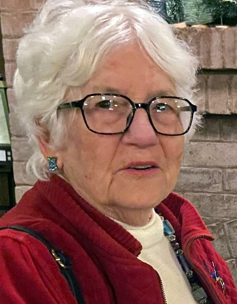 A woman with white hair, glasses and a red jacket