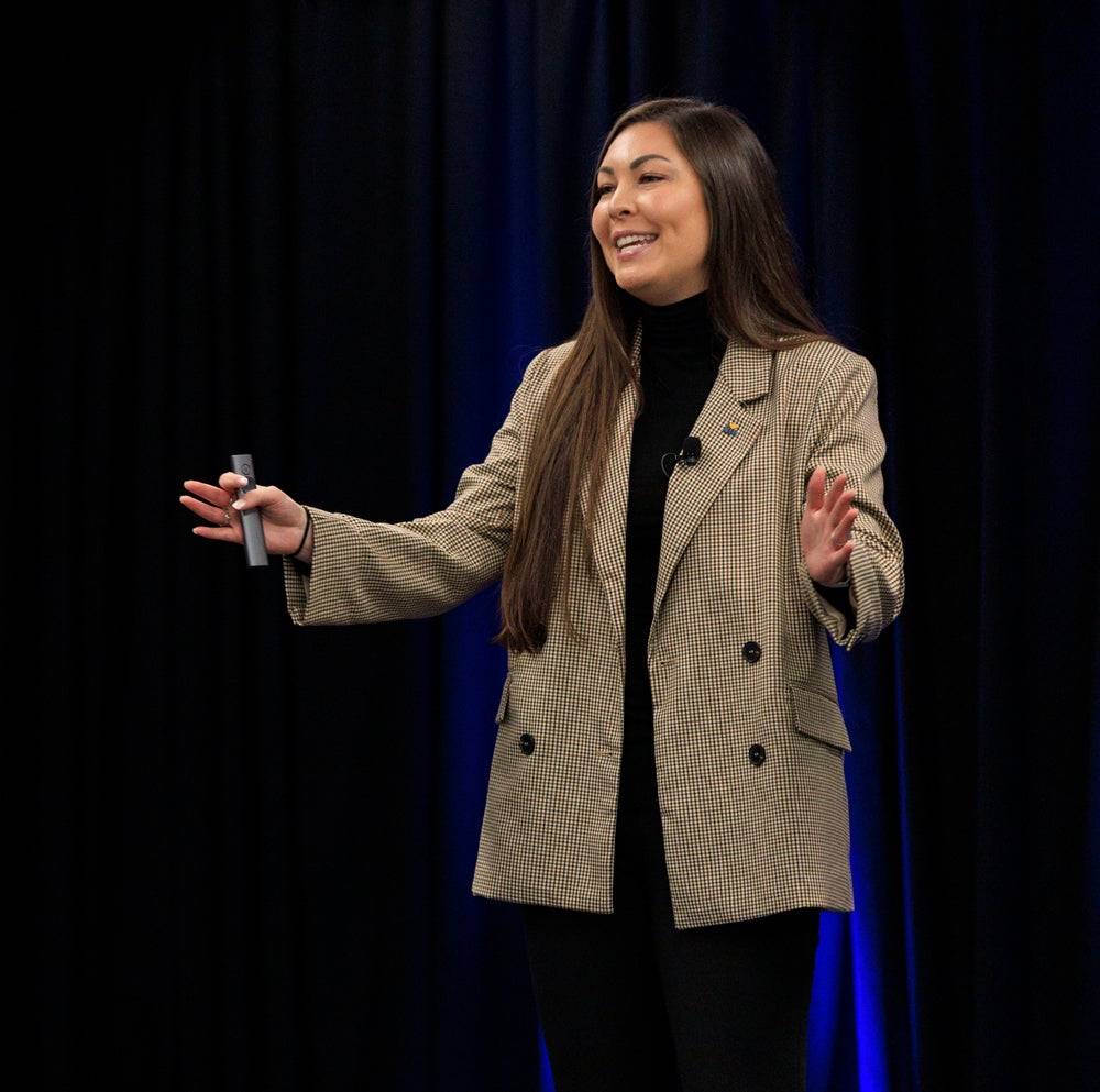 A woman wearing a suit gesturing while talking on a stage