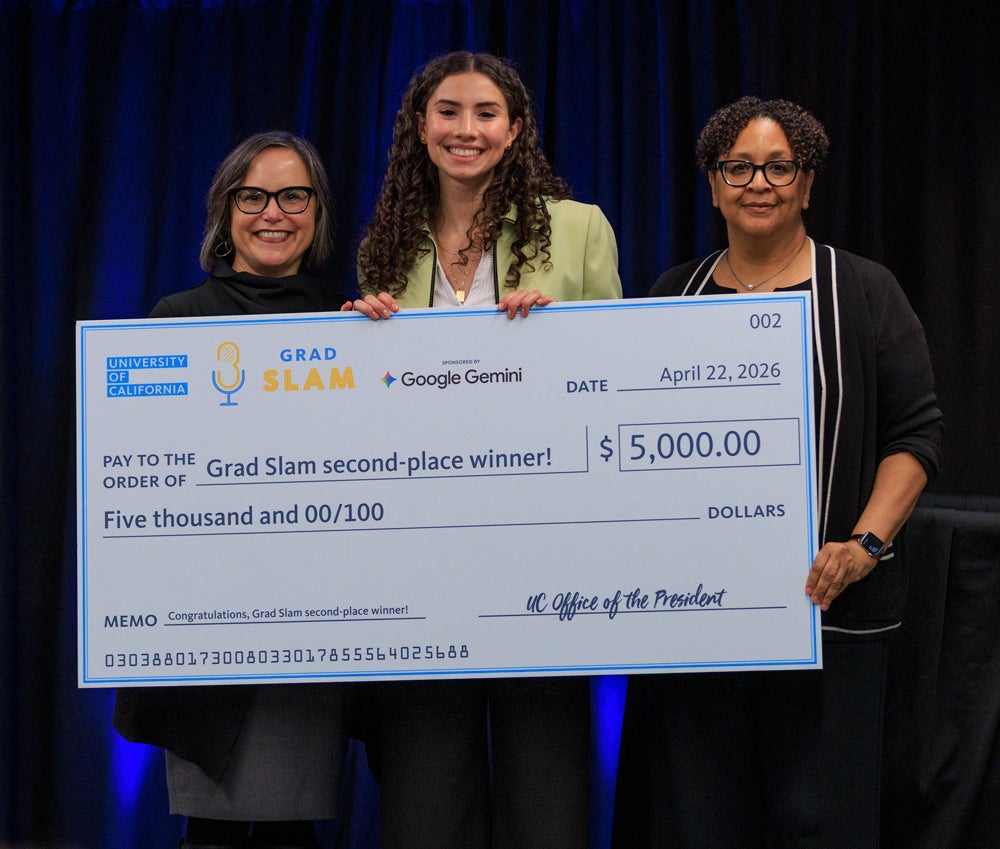 Three women standing together holding a giant prize money check