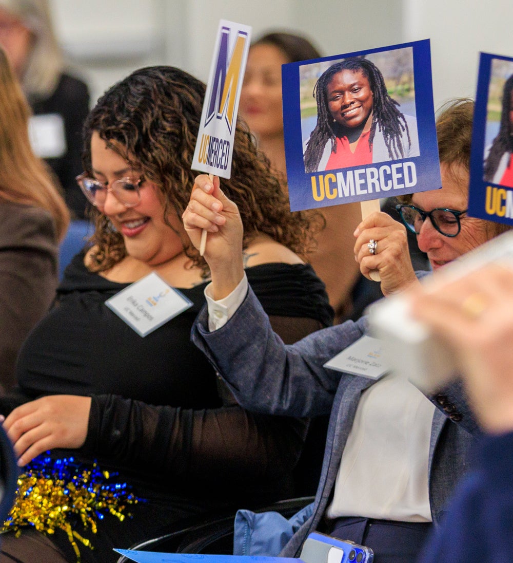 Grad Slam audience members from UC Merced holding signs for their contestant