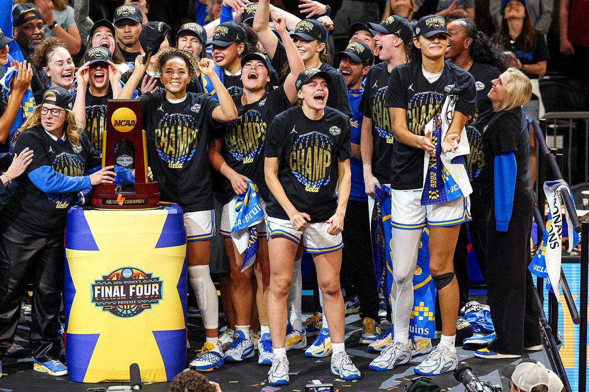 In champ T-shirts, the UCLA women's team stands on a podium together with the trophy