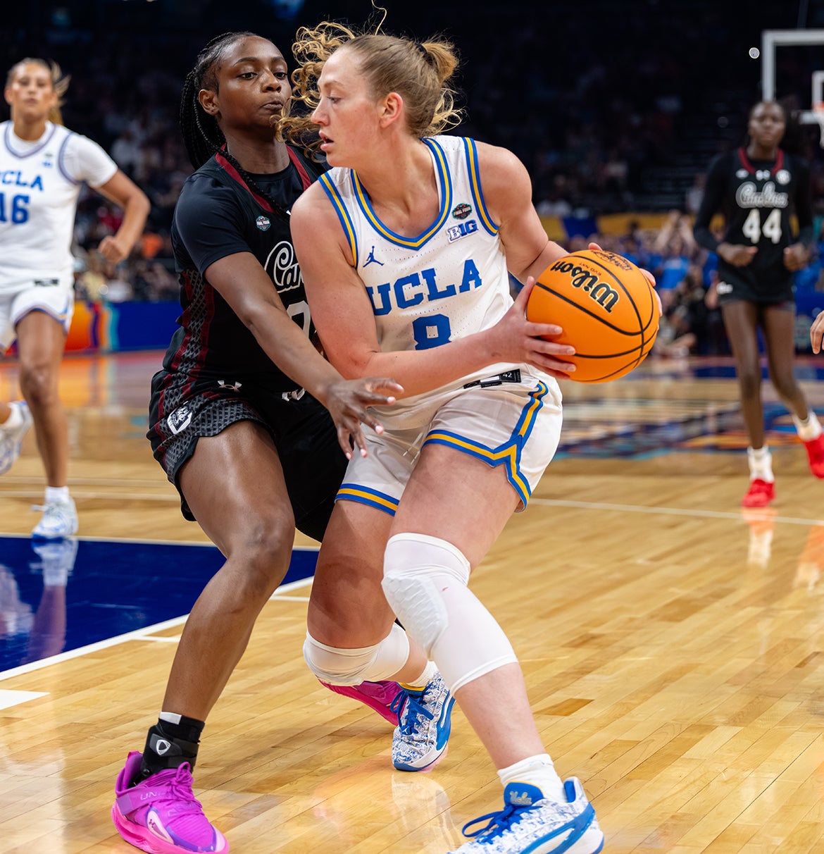 A UCLA woman basketball player holds the ball while being guarded closely by a South Carolina player