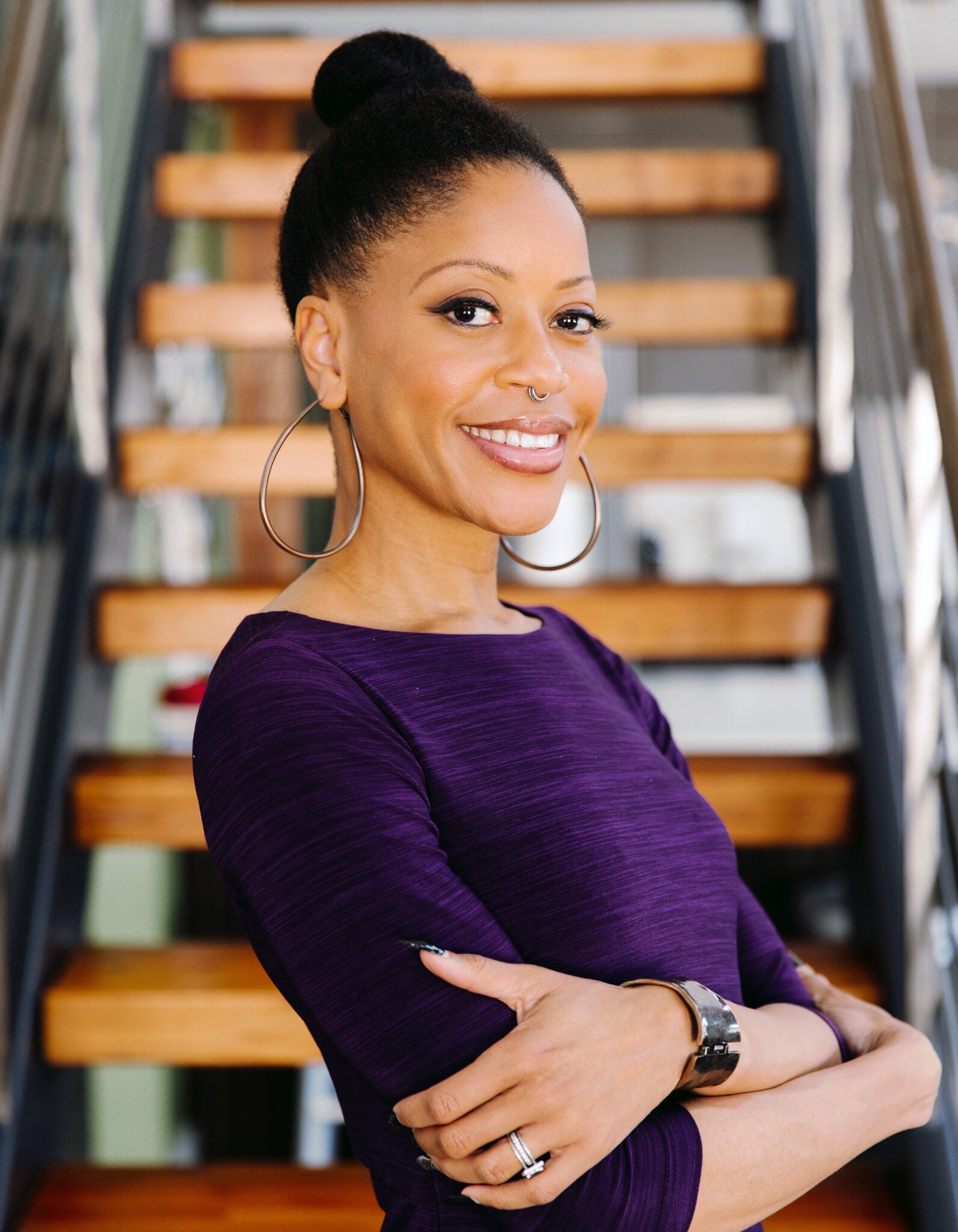 Woman in purple top smiles with arms crossed