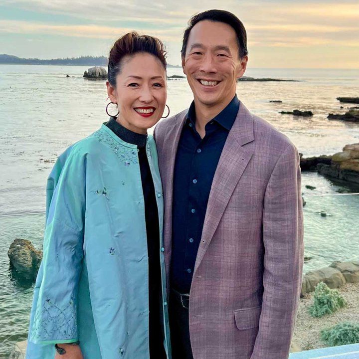 Two people pose together for a picture in front of water at sunset