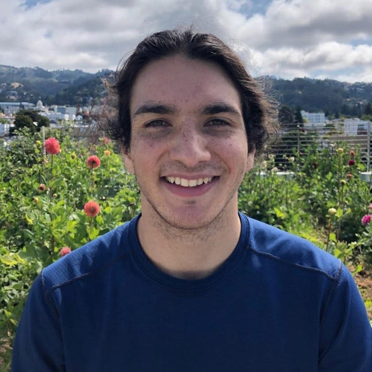 A man with a dark blue shirt in front of flowers