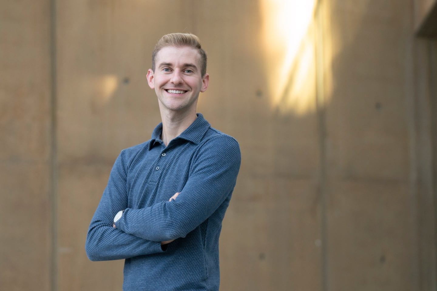 A man in a blue shirt stands with his arms crossed