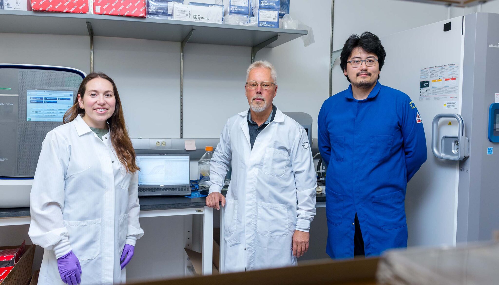 Three people in lab coats stand in a lab