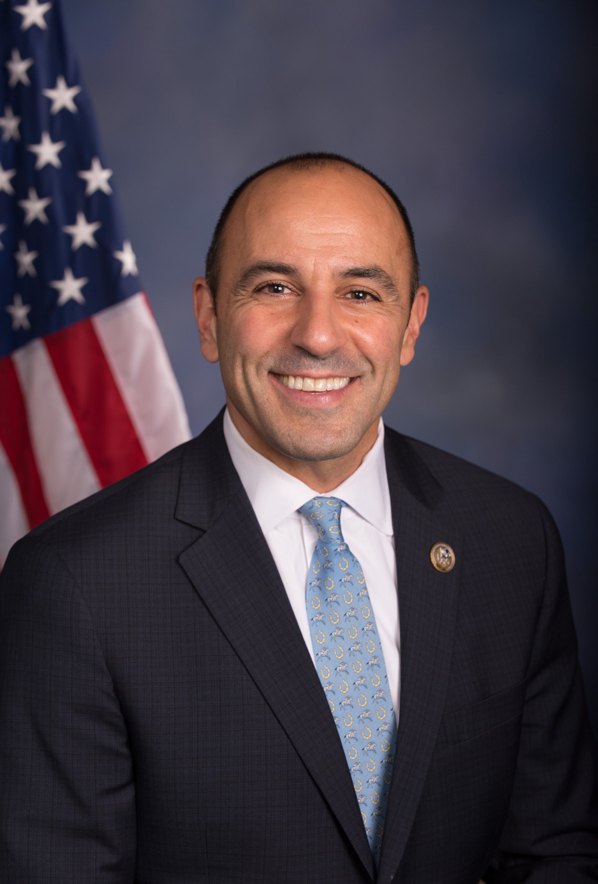 A smiling man in a suit and tie in front of the American flag