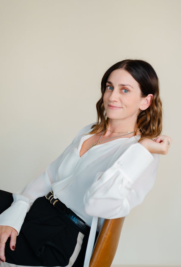 Woman in white blouse looks at camera from chair
