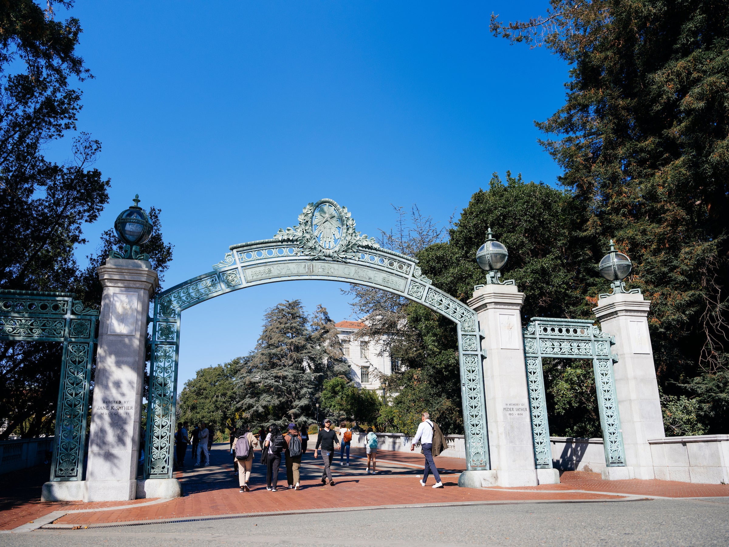 The green Sather Gate on the UC Berkeley campus with people walking under it on a clear day