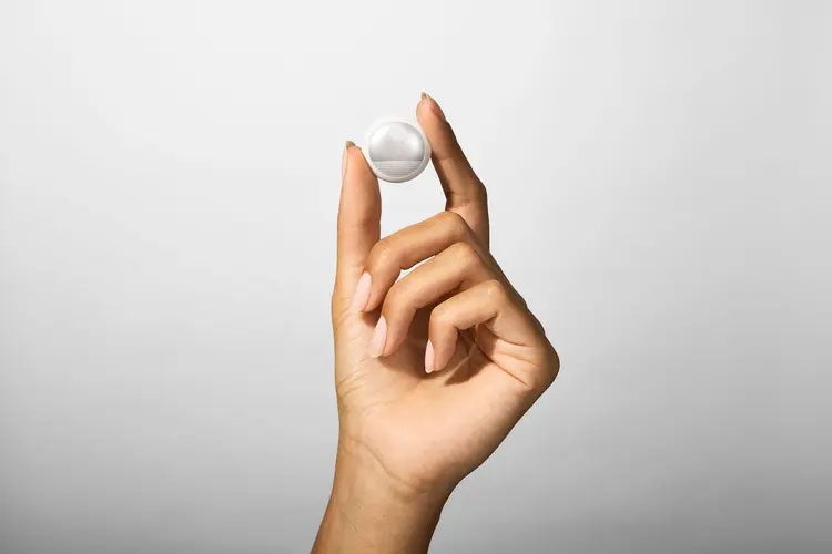 A hand holds a small, round white wearable sensor against a light background.