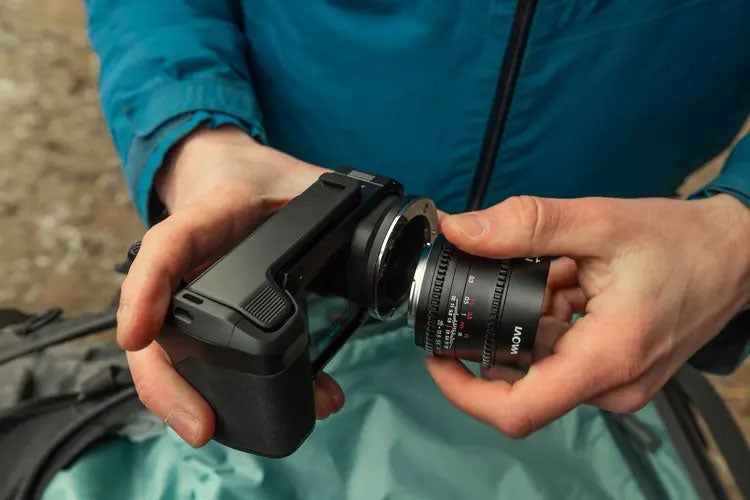 Close-up of hands attaching a camera lens to a compact black camera.
