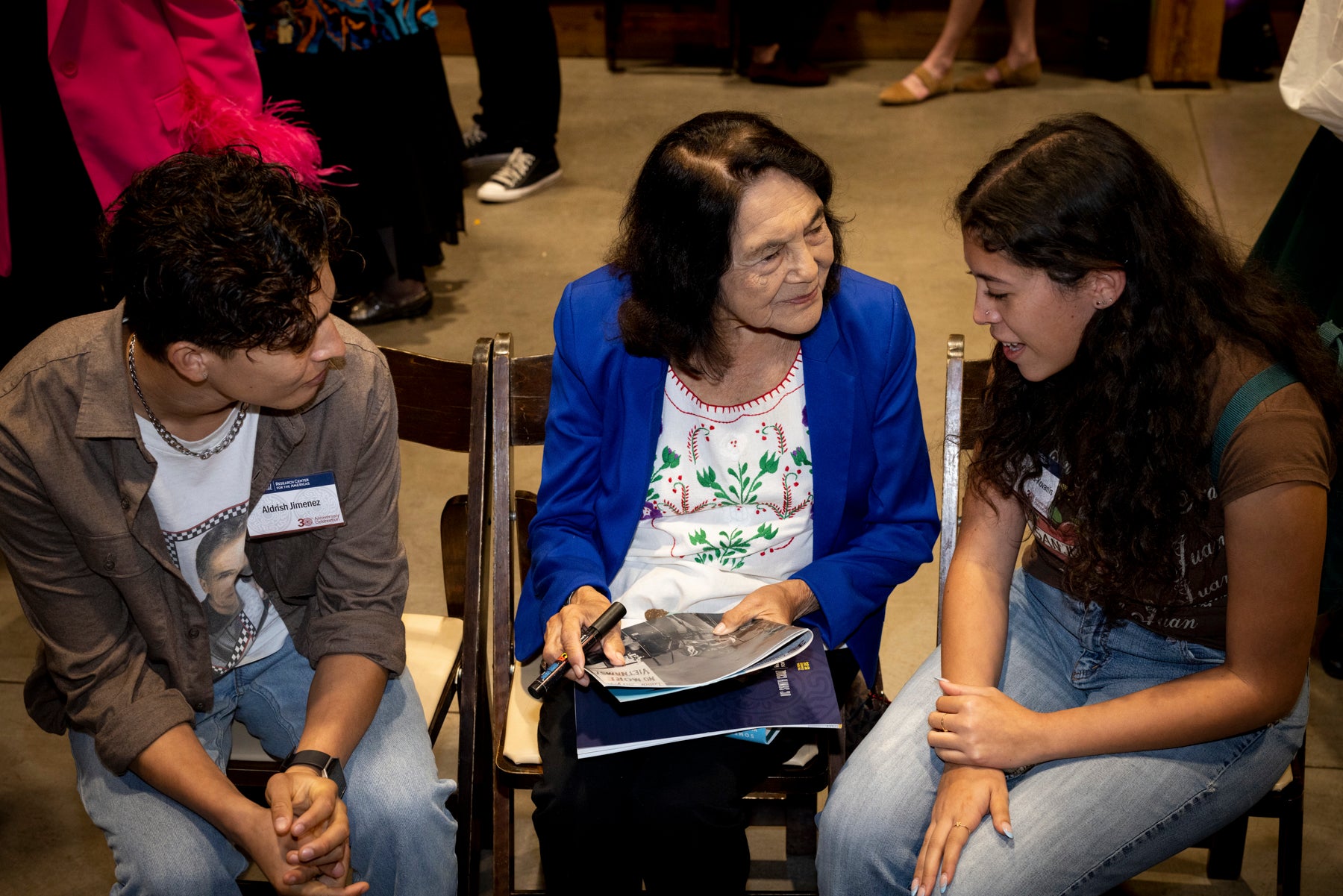 Two students sit on either side of Dolores Huerta