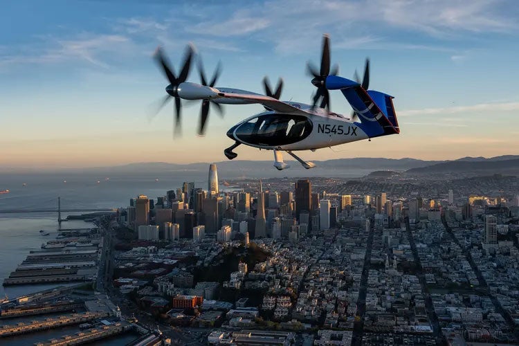An electric air taxi flies above San Francisco at sunset.