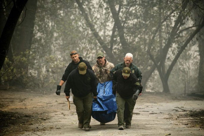 Men carrying a body bag out of a burnt area