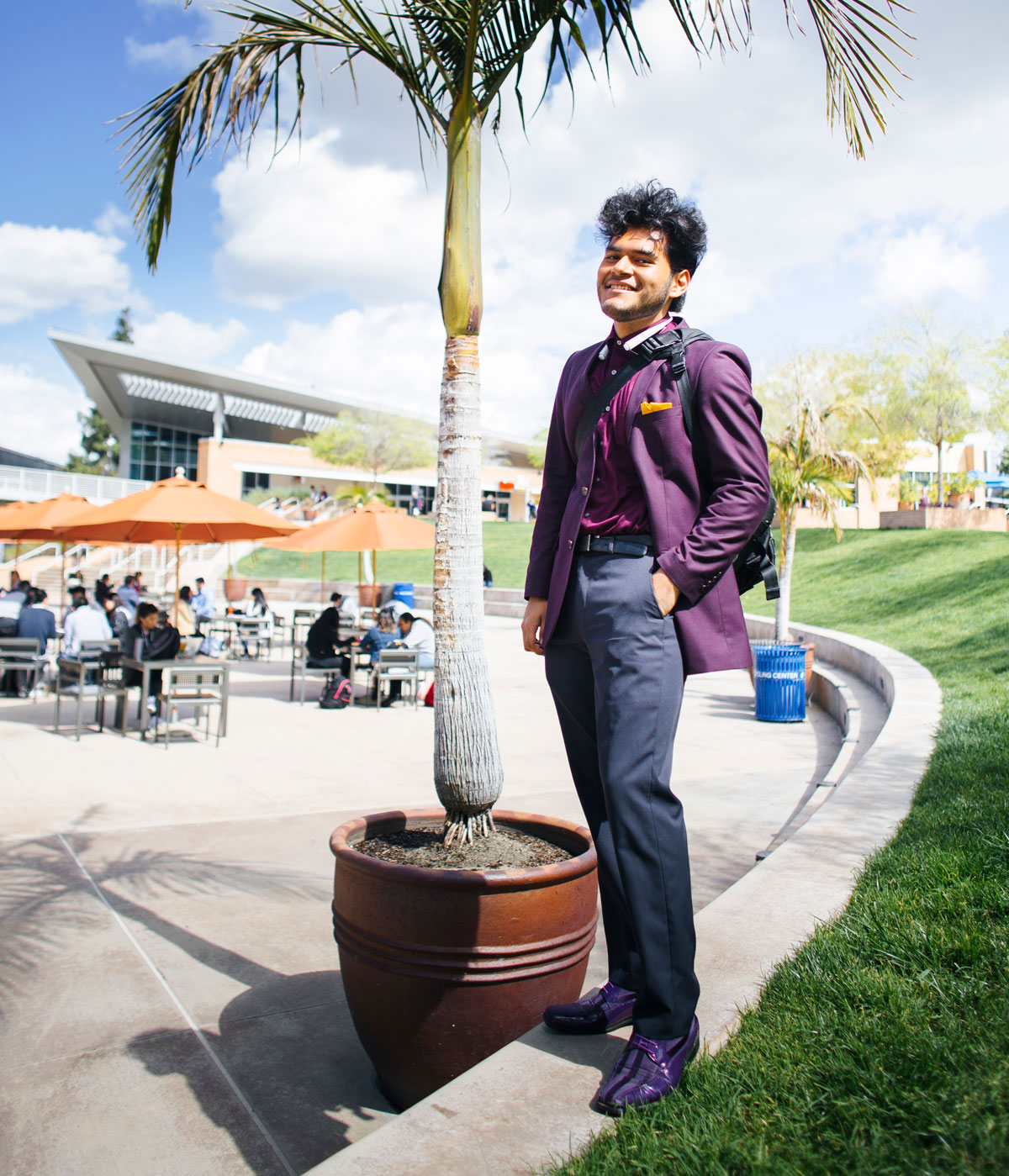 Man in purple suit poses for picture under palm tree