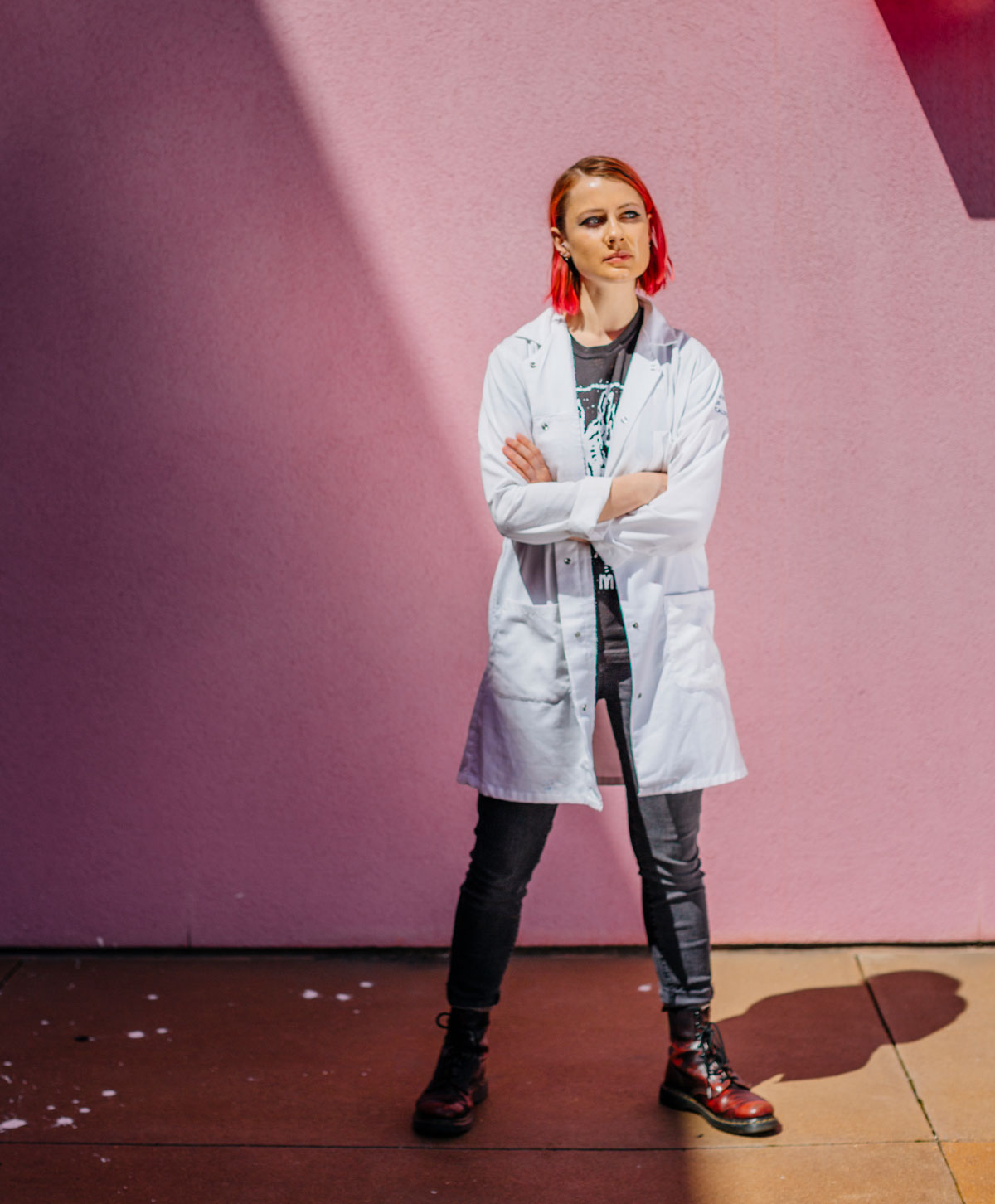 Female student in lab coat and combat boots in front of a pink wall