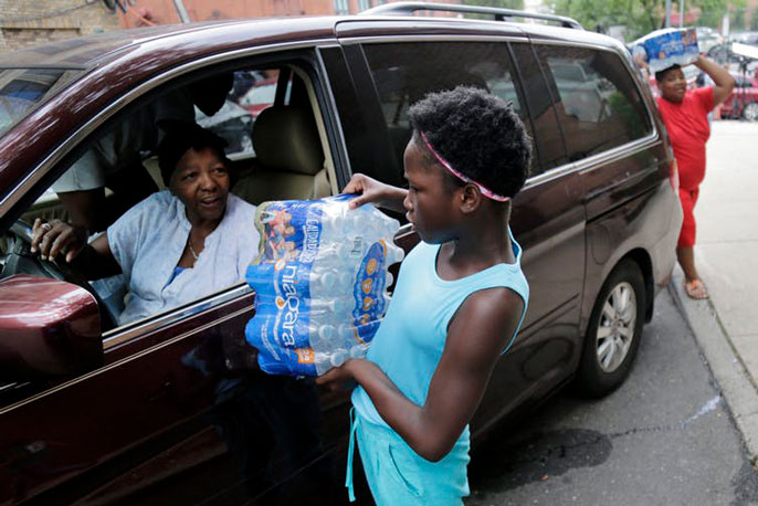 A child holding bottled water speaking to an adult in a car