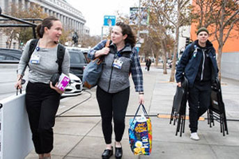 Three nursing team members carrying equipment on Fulton Street