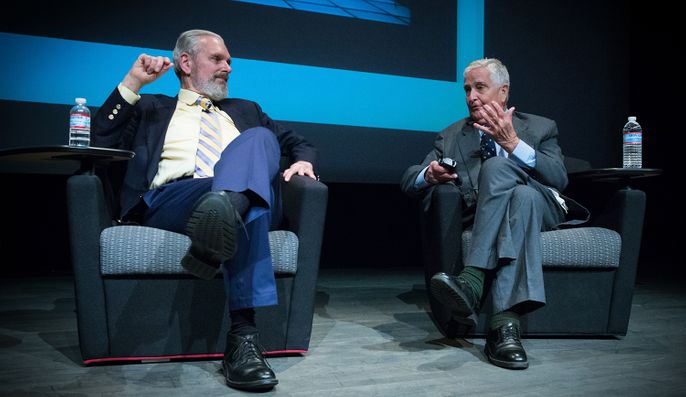 two men sit on a stage