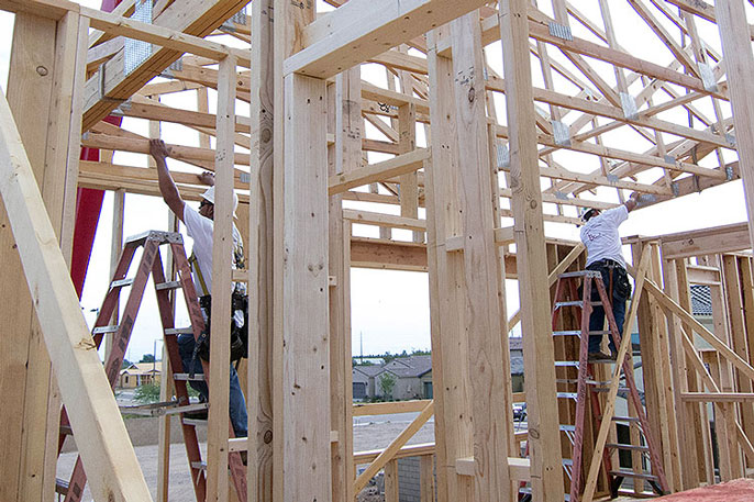 Construction workers on ladders building the frame of a house