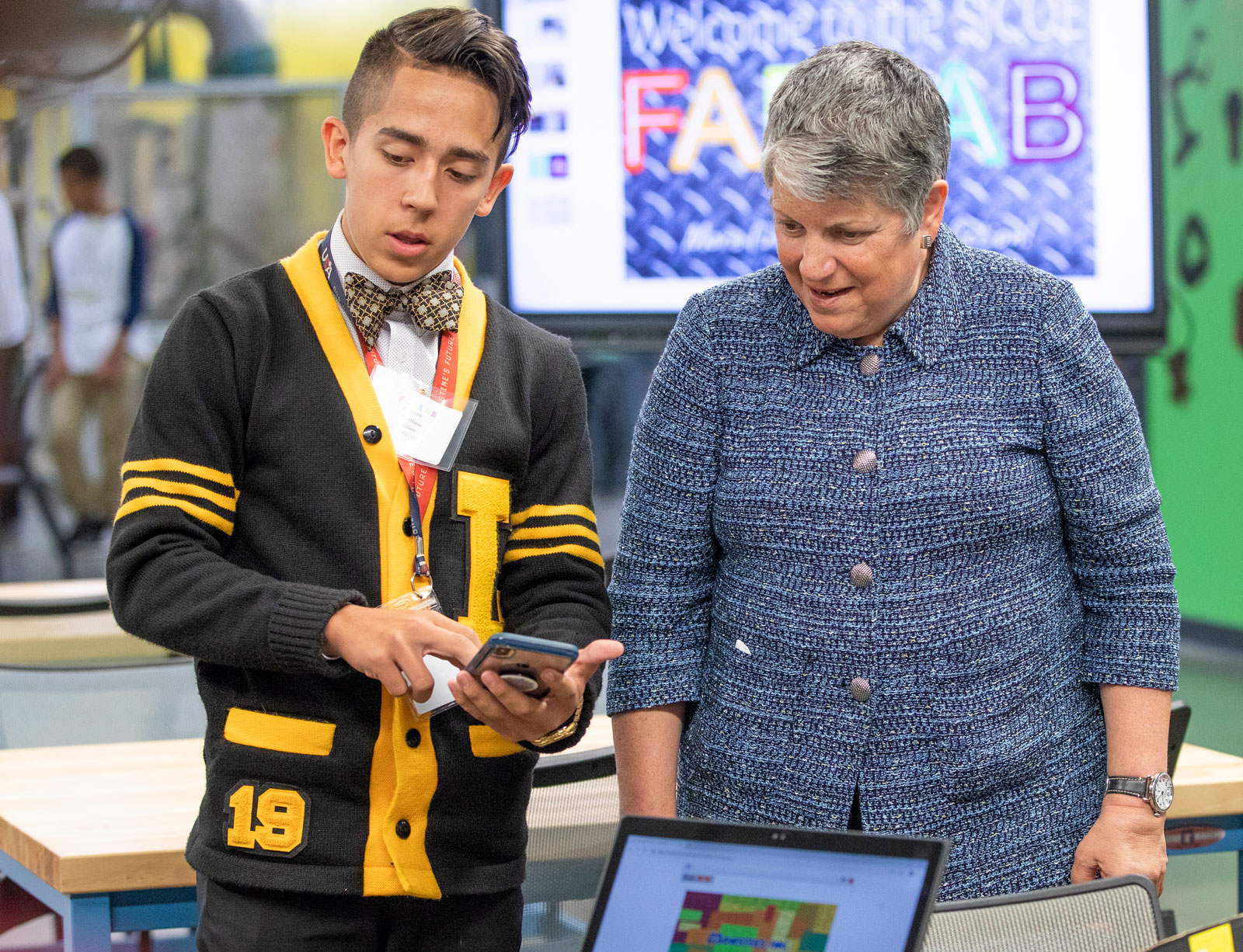 UC President Janet Napolitano stands with a teenager who shows her something on a phone