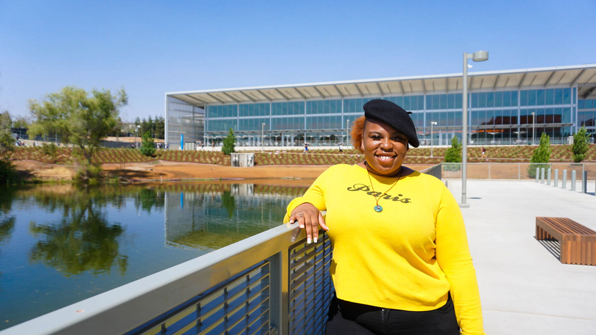 Female student with beret and bright yellow sweater smiles at camera