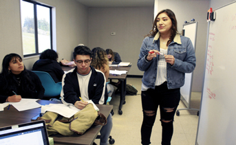 Young woman in classroom in front of white board, other students at tables