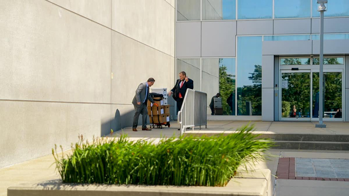 Men in suits move large boxes of documents around outside a courthouse